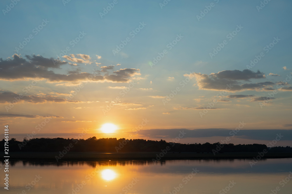 Fototapeta premium Sunset sky over calm lake with reflection and dark tree line, tranquil evening landscape