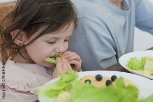 Fotografía A close-up of a toddler girl focusing on eating a fresh green lettuce salad during lunchtime at home