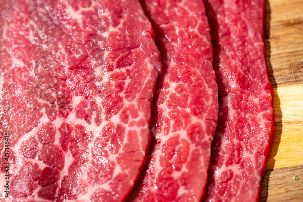 Obraz premium Raw beef steaks with natural fat marbling. Raw beef slices prepared for cooking. Close-up raw beef texture with intramuscular fat. Fresh raw beef on wooden cutting board.