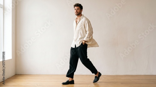 Full length portrait of a stylish young man walking in a bright minimalist studio