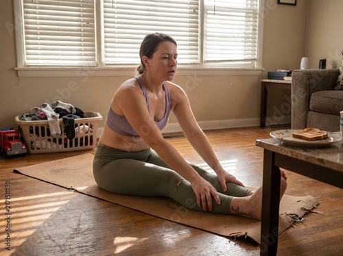 Woman stretching on worn cork yoga mat in lived-in apartment with morning blind-light shadows, authentic wellness