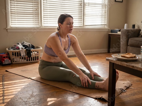 Woman stretching on worn cork yoga mat in lived-in apartment with morning blind-light shadows, authentic wellness