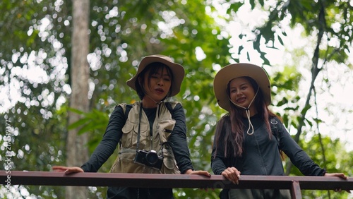 Картината върху платно Asian female hikers standing on wooden bridge walkway and enjoying scenic green forest
