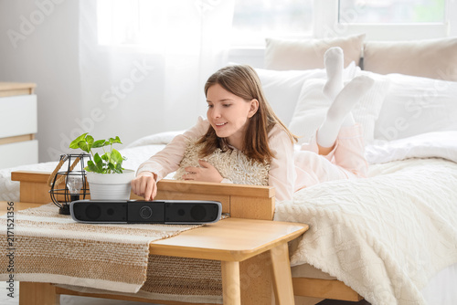 Young happy woman turning on wireless portable speaker at home