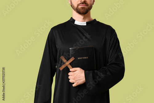 Bild auf Leinwand Young male priest with holy Bible and wooden cross on green background, closeup