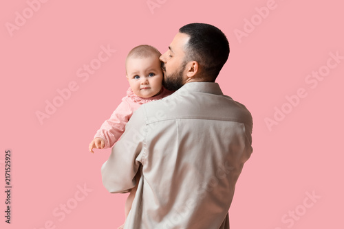 Happy young father kissing his cute little baby on pink background