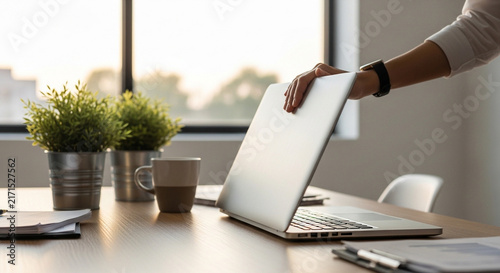 Person closing a laptop on a modern office desk at sunset