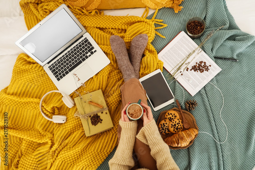 Beautiful young woman with cup of coffee, books and devices lying on bed at h...