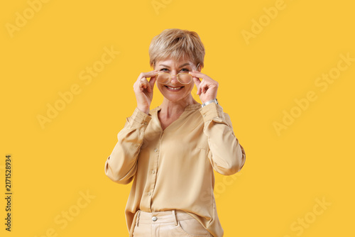 Mature businesswoman in eyeglasses on yellow background