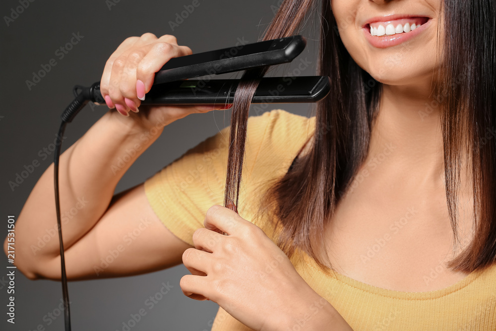 Obraz premium Beautiful young woman straightening hair on grey background, closeup