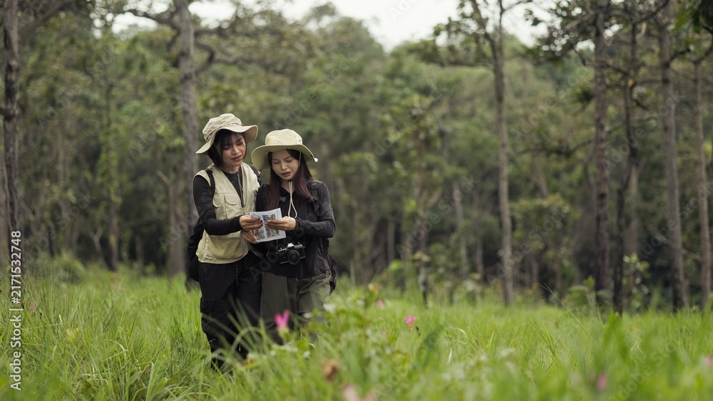 Fototapeta premium Asian Female Travelers Walking With Paper Map In Wildflower Meadow