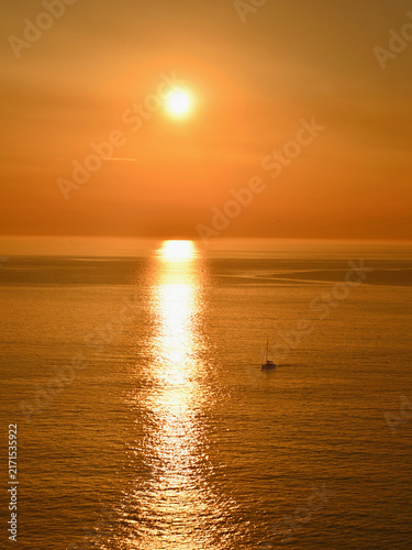 Photography Golden reflections of the sunset over the ocean, with a pleasure boat returning to port