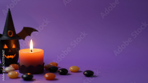 Halloween pumpkin candle witch hat orange purple background glowing flame create warm still life with orange light, purple color, and soft candle shadow