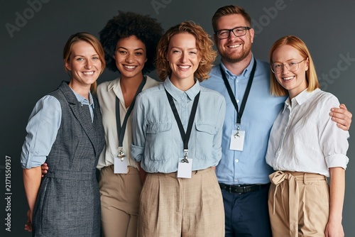 Group of smiling diverse colleagues wearing identification badges standing together in studio