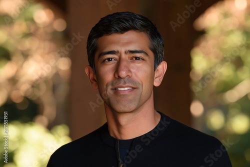 Smiling indian man in black sweater looking ahead with warm outdoor background lighting