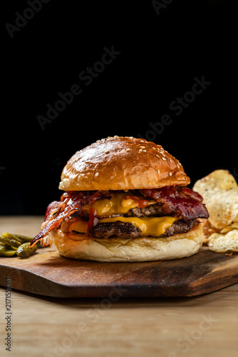 Loaded double crispy bacon cheeseburger with melted cheese, no vegetables, black background