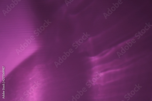 Abstract dark purple background with diagonal neon pink light refractions and soft wavy shadow overlays. Ideal textured backdrop for modern aesthetic design projects.