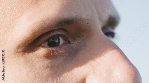 Close-up of a person's eye with sunlight reflecting against it during a clear day outdoors