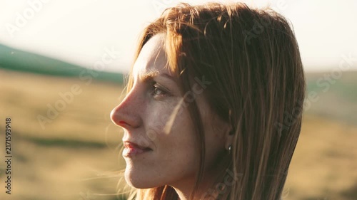 Woman stands in grassy field during sunset looking towards the horizon with soft light hitting her face