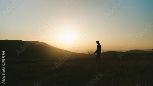 Two people walk on a hillside during sunset near mountains in the background
