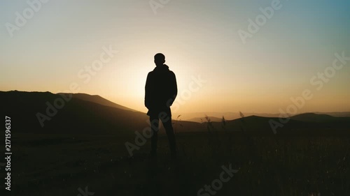 Person stands on a hill at sunset looking towards the horizon with mountains in the background and a clear sky