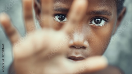 A Boy's Plea for Attention: A young boy looks directly at the camera, his open hand held up in a gesture that conveys a sense of urgency and a silent request for understanding.
