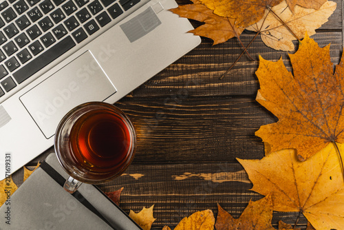 Cozy workspace with laptop, tea, and autumn leaves on wooden desk