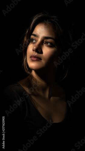 Cinematic photorealistic portrait of a beautiful South Asian woman illuminated by a dramatic single spotlight against a deep black background.