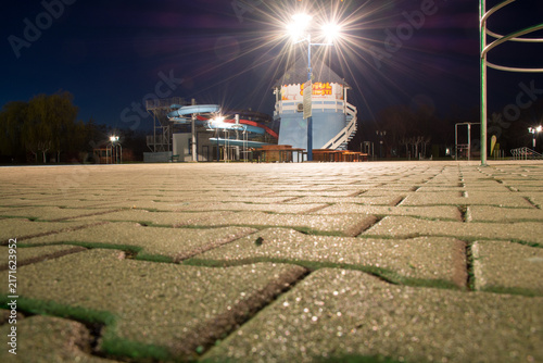 Konstfotografi Night view of an empty park with brightly lit water slide and textured paving stones