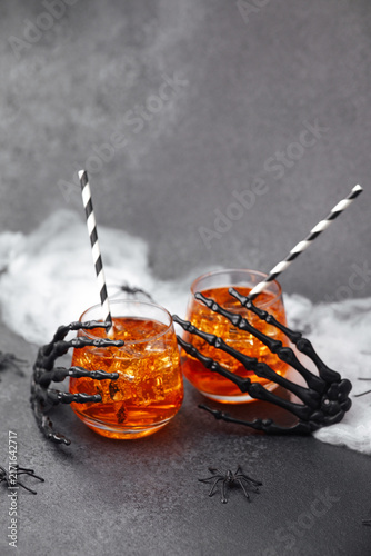 Obraz na płótnie Spooky skeleton hands holding orange drinks with straws and cobwebs, on a dark s