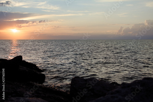 Canvas Print Peaceful ocean sunset with vibrant sky reflecting on waves, silhouetted rocky foreground, and soft orange and pink hues blending into calming blue horizon