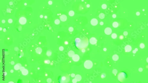 Particles of glowing light floating across a vibrant green screen backdrop form a dynamic abstract pattern.