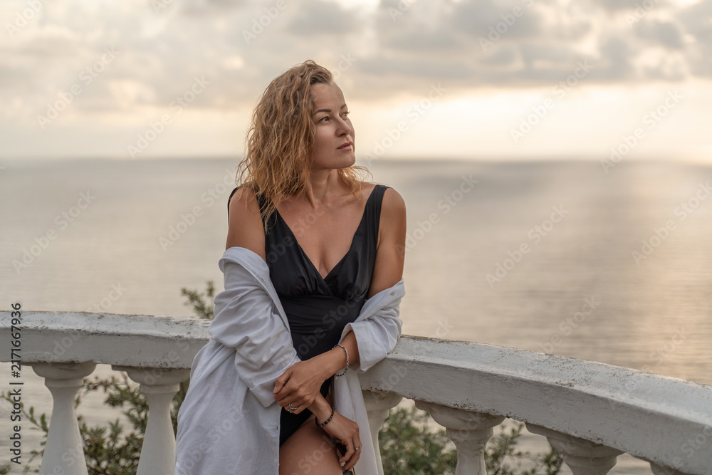 Fototapeta premium Woman leaning on terrace railing enjoying tranquil ocean view during late afternoon light
