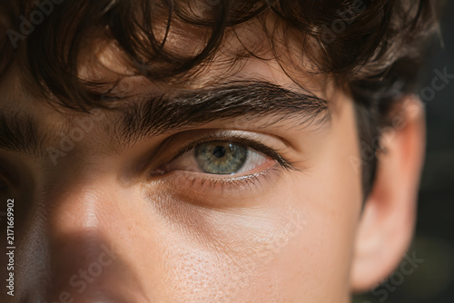 Detailed close-up portrait of a human green eye framed by dark hair, capturing focus, emotion, perception, and natural facial texture.