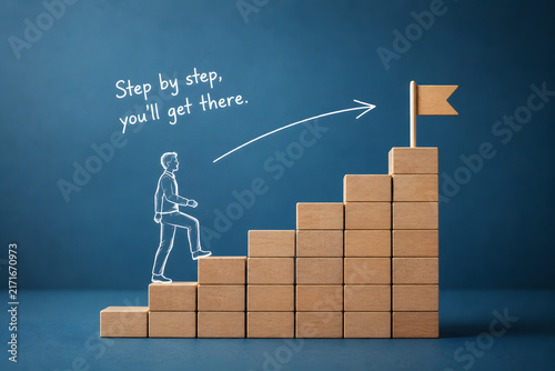 Wooden blocks form a rising staircase as a person climbs toward a flag, symbolizing progress, ambition, career growth, and achievement.