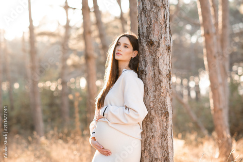 Pregnant woman 30-34 year old wearing knitted maternity clothes posing outdoors over autumn nature background. Motherhood.