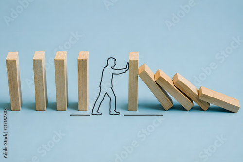 Wooden blocks show a person stopping a chain reaction, symbolizing risk prevention, timely intervention, resilience, and problem solving.