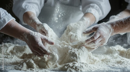Multiple hands, wearing white sleeves, actively knead a large mound of white flour and dough on a dark kitchen surface, demonstrating the collaborative baking process.