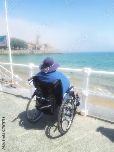 The daily dream of an elderly, disabled person in a wheelchair, gazing at the sea on the San Lorenzo beach promenade in Gijón.