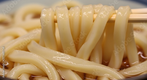 Udon noodles are lifted with wooden chopsticks from a traditional broth in a ceramic bowl.