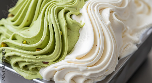 Gelato swirls of pistachio and vanilla cream are presented in a cold metal serving container.