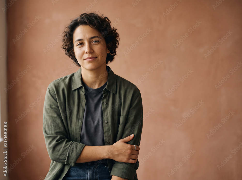Obraz premium Emotional studio portrait of a non-binary person looking confidently toward the camera, subtle reflective expression, minimalist warm background
