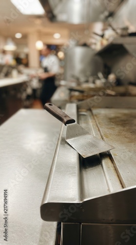 Stainless Steel Spatula Resting on a Commercial Griddle in a Busy Restaurant Kitchen Environment for Culinary Gastronomy and Food Preparation