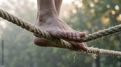 Barefoot person balancing carefully on thick rough rope outdoors during soft morning golden hour natural light