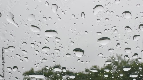 Raindrops Merge and Flow Down Glass with Blurred Trees and Copy Space