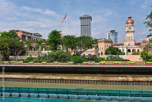 Historical Sultan Abdul Samad Building with clock tower by the Klang River in Kuala Lumpur, Malaysia with the Malaysian national flag flying under a bright blue sky