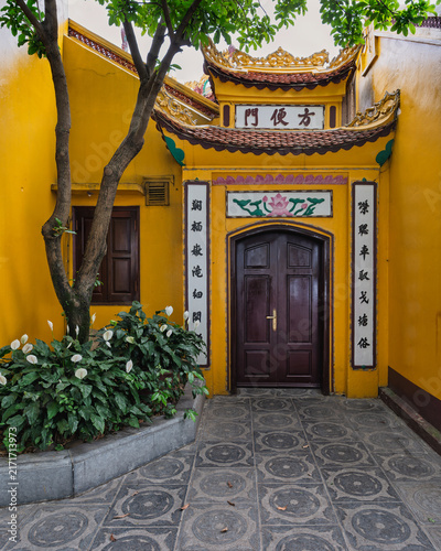 Yellow traditional wall with a wooden door and peace lilies next to a tree at Tran Quoc Pagoda in Hanoi, Vietnam