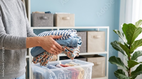 Person holding stack of folded clothes and organizing wardrobe at home. Seasonal closet change with summer clothes. Housework chores, laundry and tidying concept for advertisement.