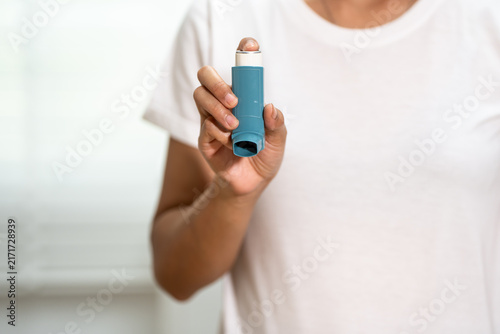Cuadro en lienzo Close-up of a woman in a white shirt holding a blue asthma inhaler, highlighting respiratory health, allergy treatment and emergency medicine