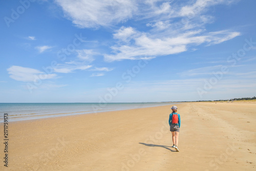 femme seule, de dos, marchant sur une plage en été.